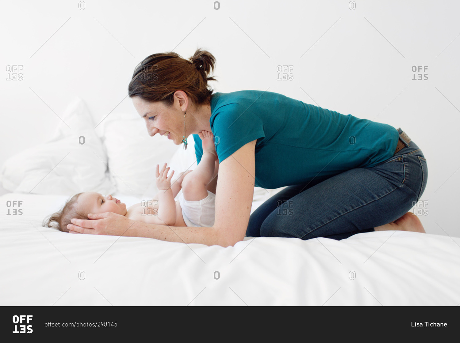 Woman kneeling over baby on bed stock photo - OFFSET