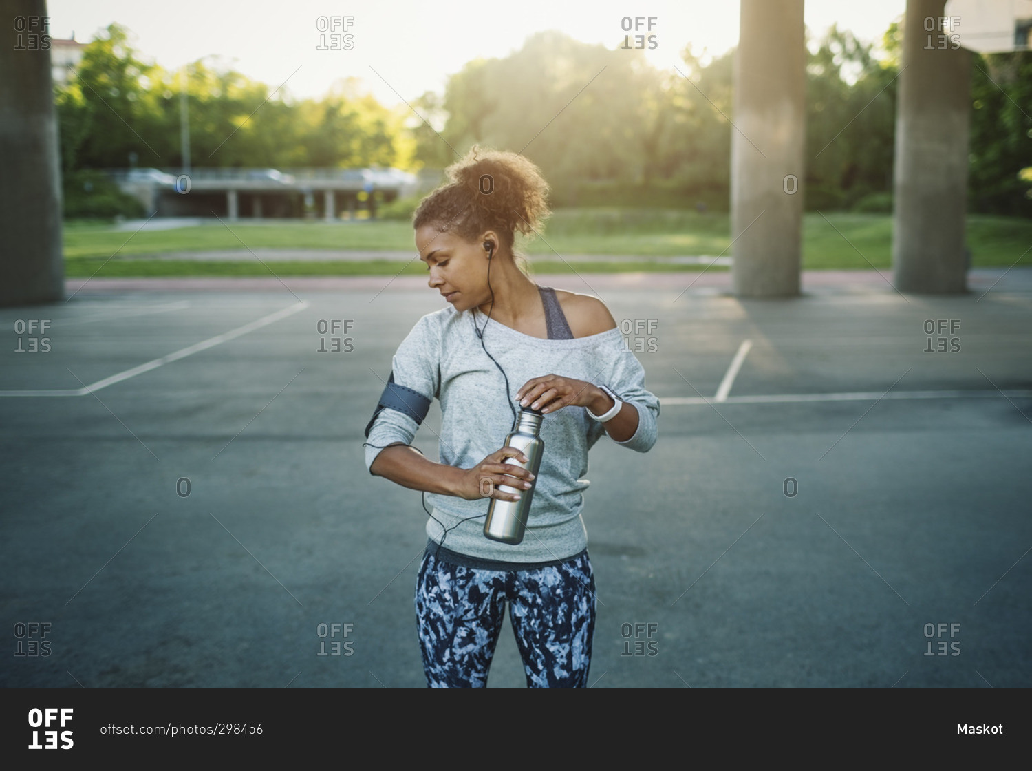 Woman holding water bottle looking down while standing on street