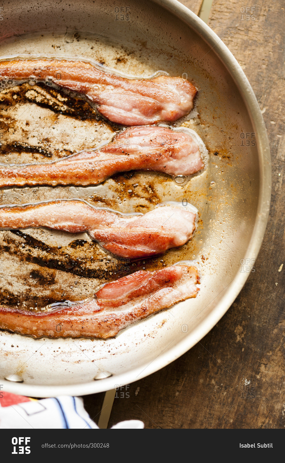 Strips of bacon in skillet on wooden table