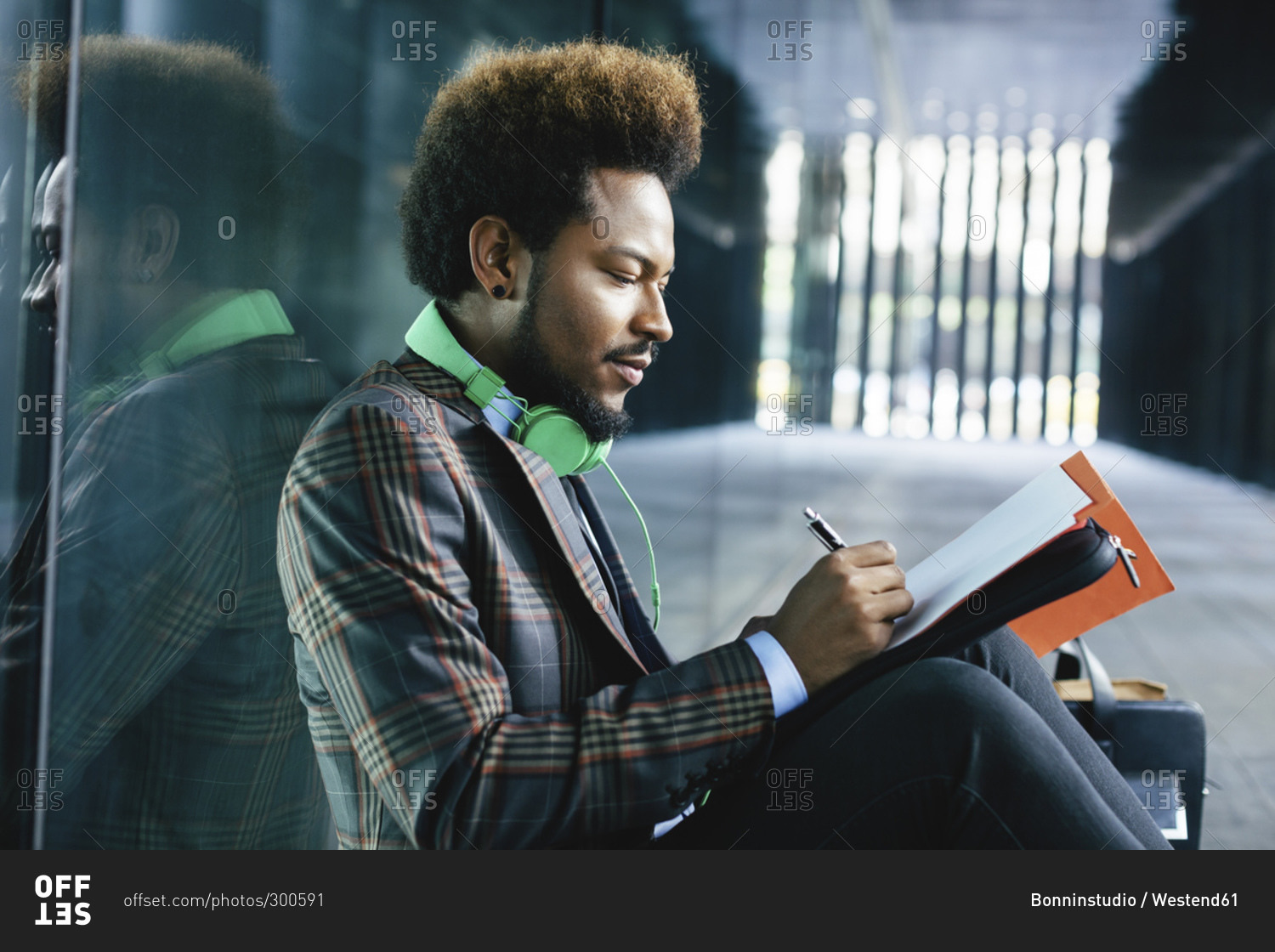 Young businessman sitting outdoors writing in folder