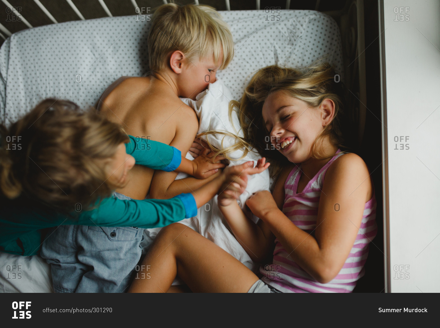 Three young siblings playing together on bed