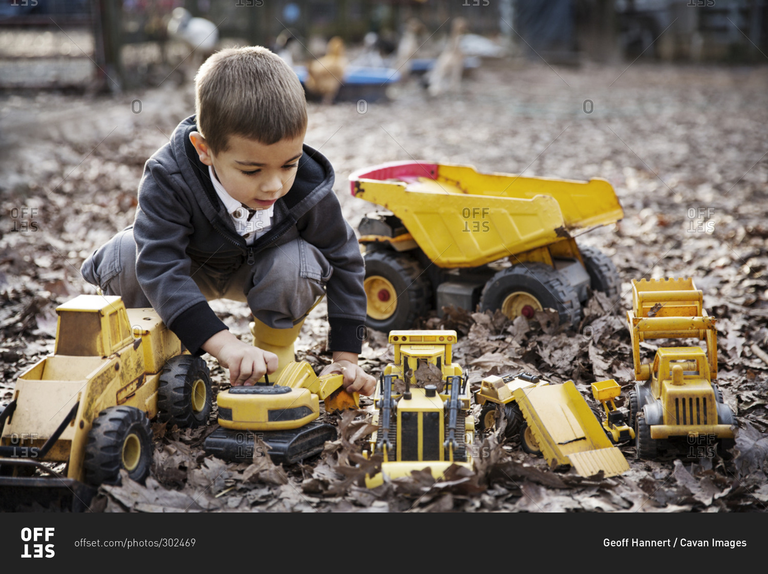 Boy playing with toy trucks in fallen leaves