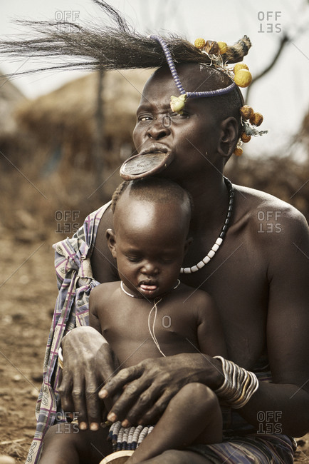 February 18, 2015: Mursi woman with lip plate holds her baby on her lap