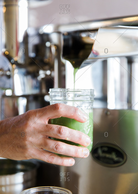 Person filling glass with green smoothie from a smoothie machine