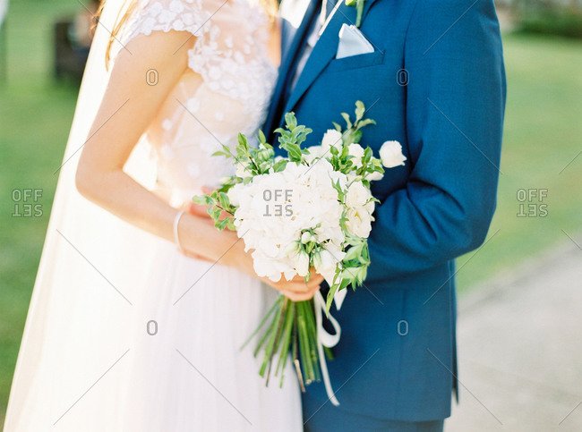 Bride holding wedding bouquet as she and groom embrace