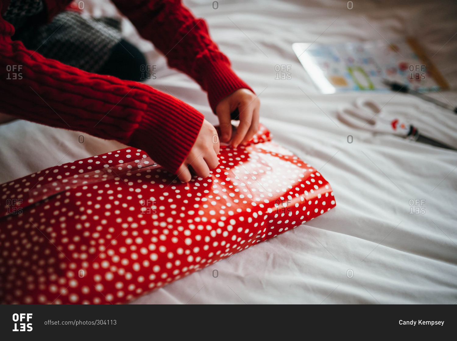 Child wrapping Christmas gift on bed