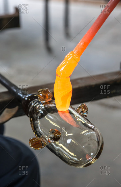 Glassblower cuts molten glass with a hand tool