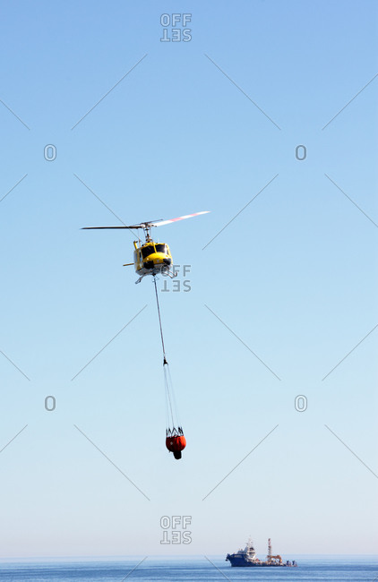 One of Cape Town's 'Working on Fire' emergency aerial fire fighting helicopters with a water bucket off Sea Point, Cape Town, South Africa
