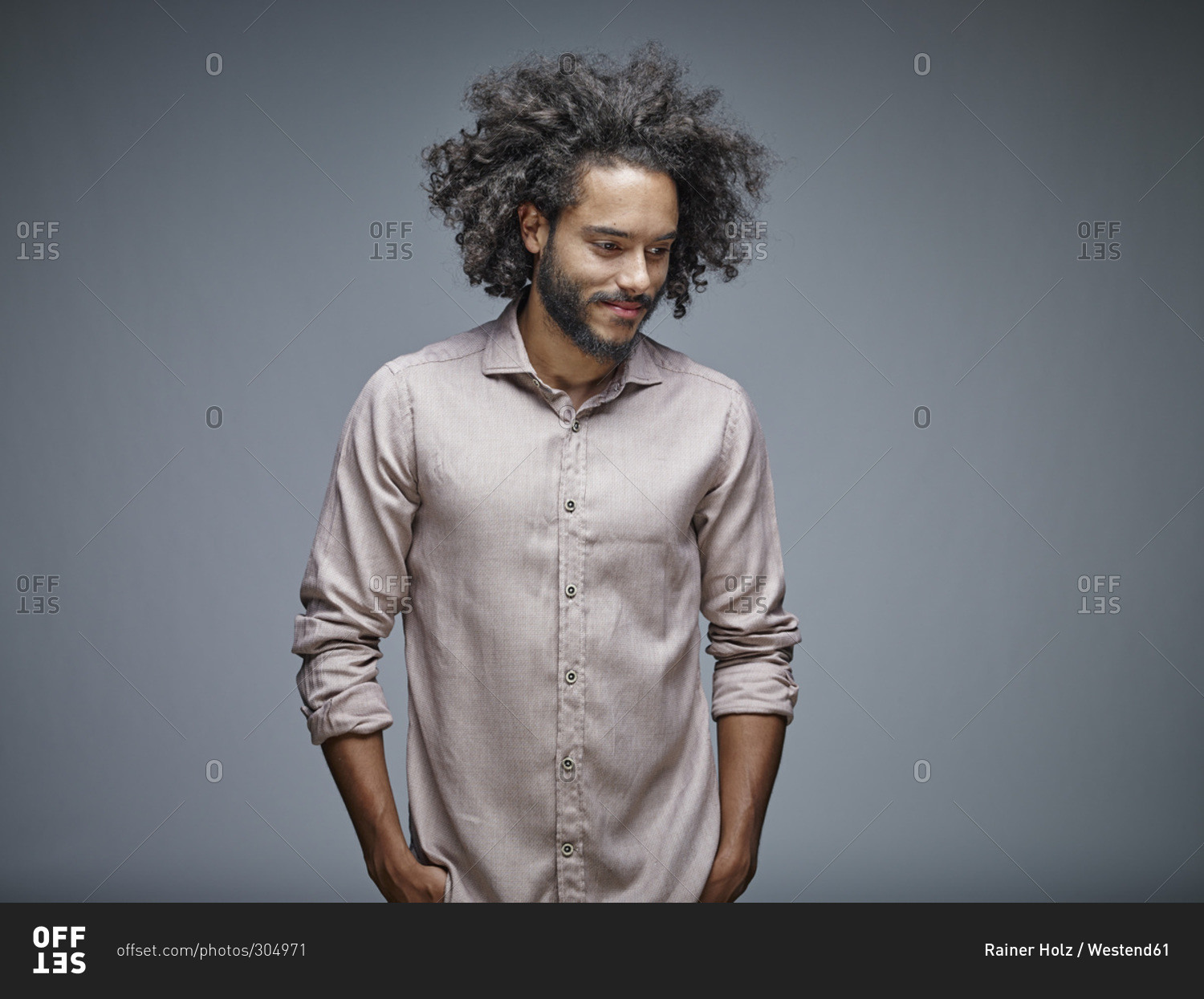 Portrait of smiling young man with curly brown hair in front of grey ...