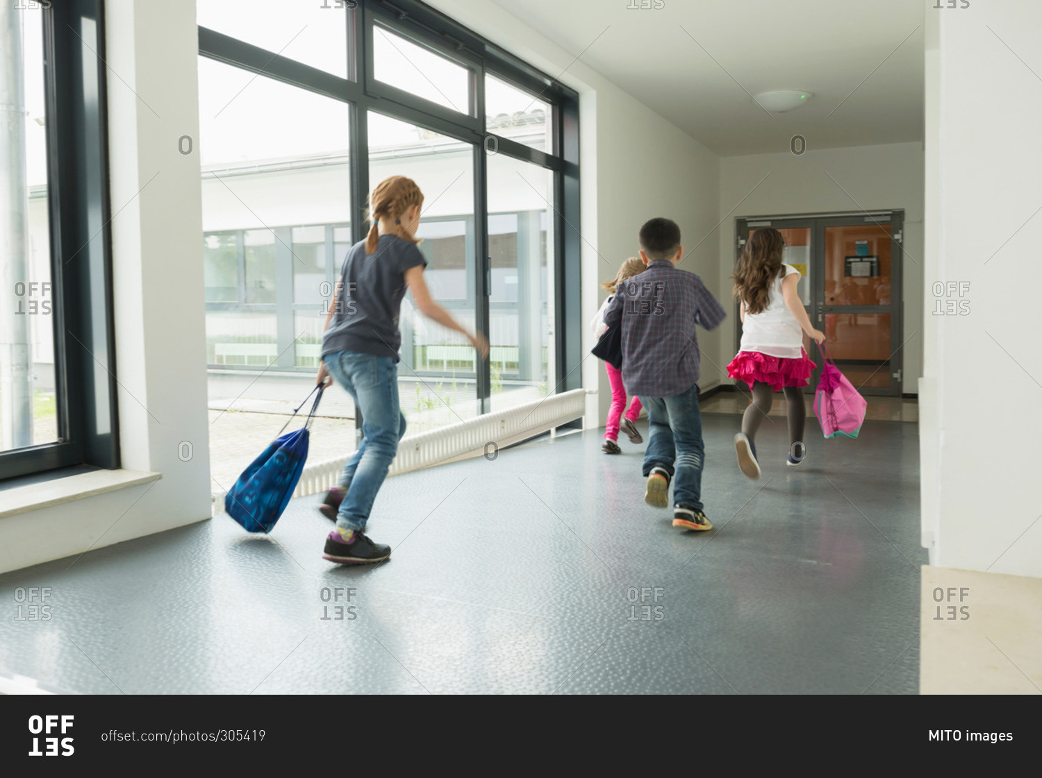 Children running with sports bags in corridor of sports hall, Munich, Bavaria, Germany