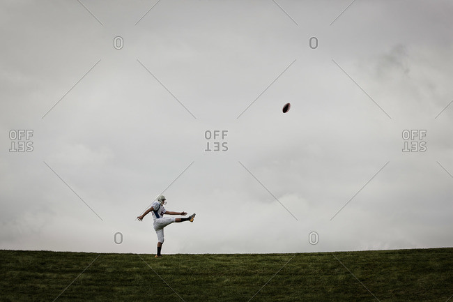 An American football player in uniform, side view, practicing his kicking