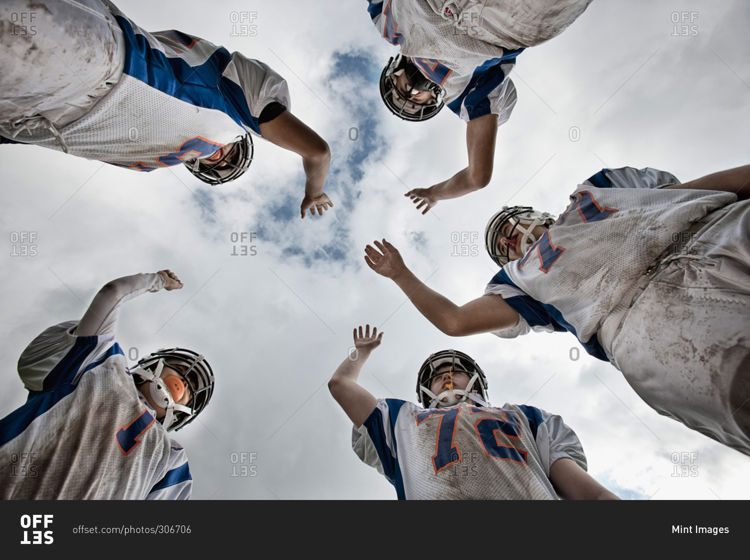 A group of American football players in sports uniform and protective helmets, in a team huddle viewed from below