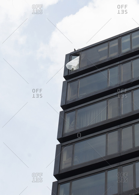 Curtain blowing out of window with bird above it on top floor of apartment building