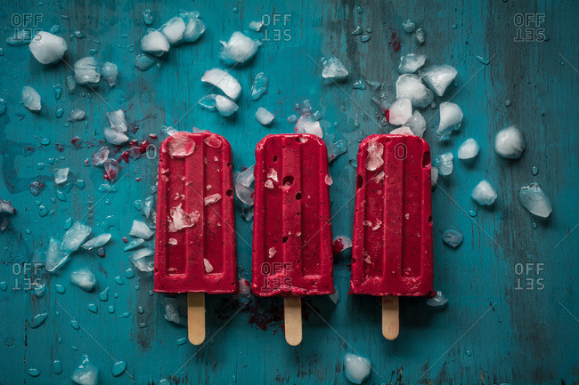 Three red popsicles with ice on blue table