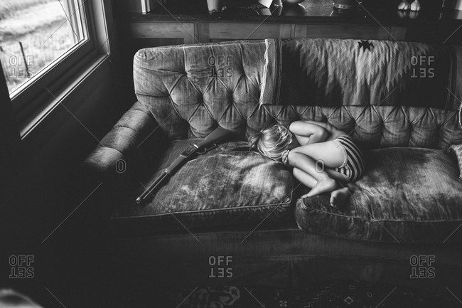 Boy Curled Up On A Couch Next To Toy Gun Stock Photo Offset