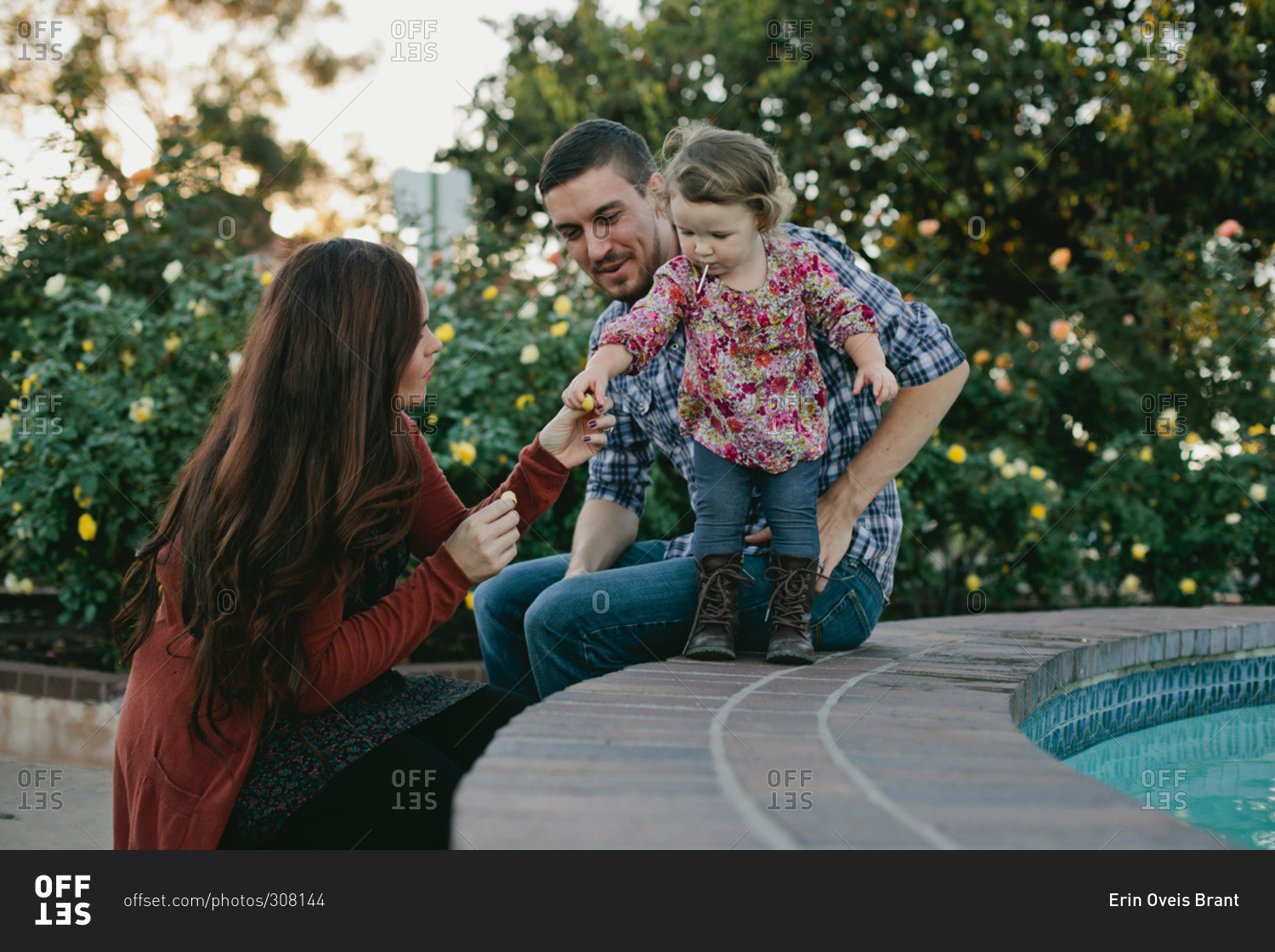 Little girl playing with her parents on the edge of a water fountain