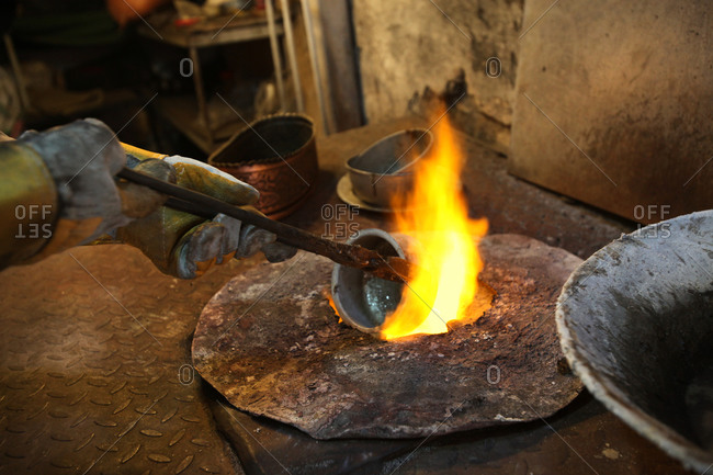 Man heating metal pot over furnace flame