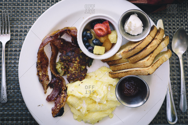 A hearty breakfast of eggs, bacon, fruit, and toast sits in natural light