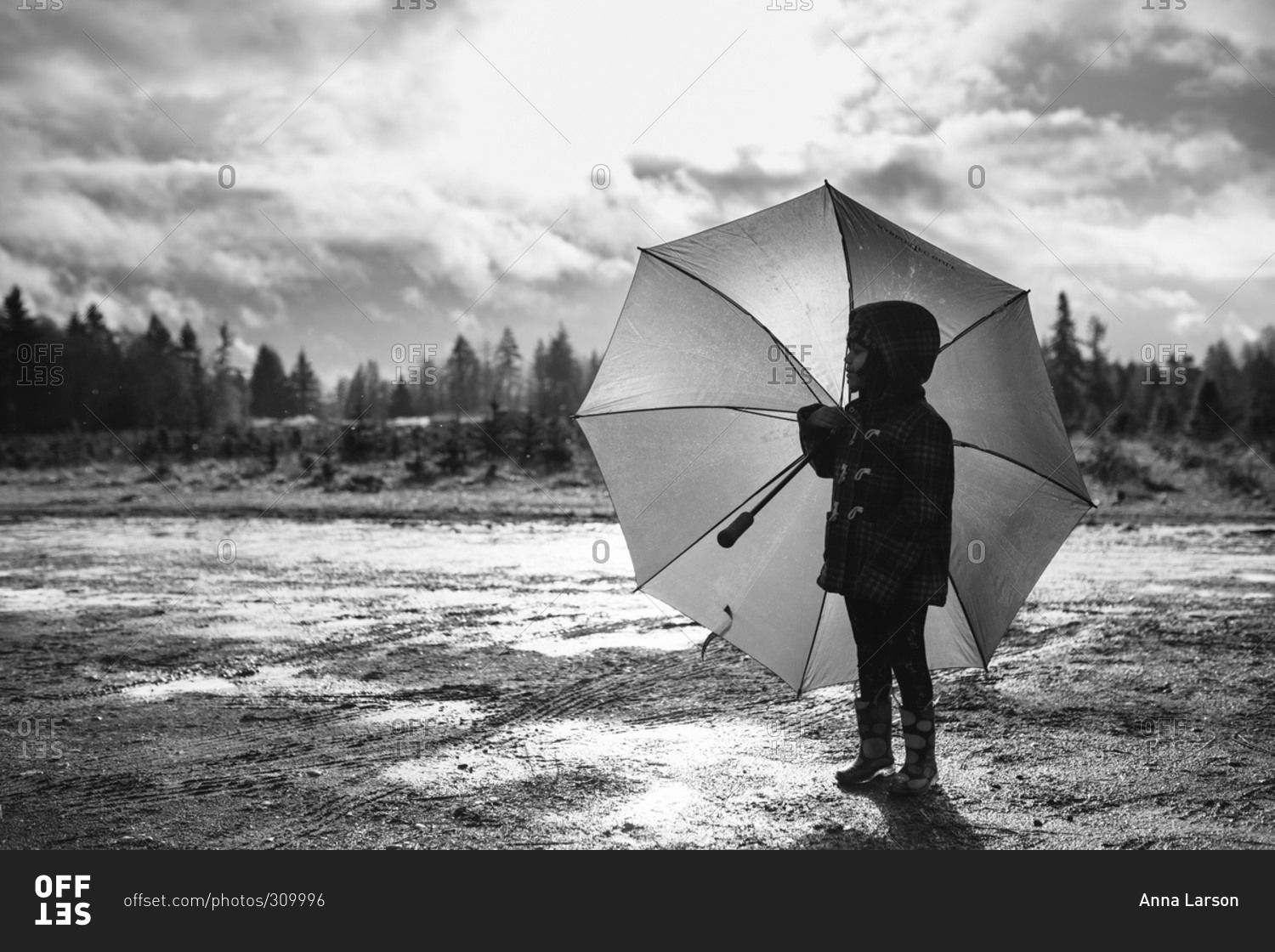 Little girl standing in a muddy field with an umbrella