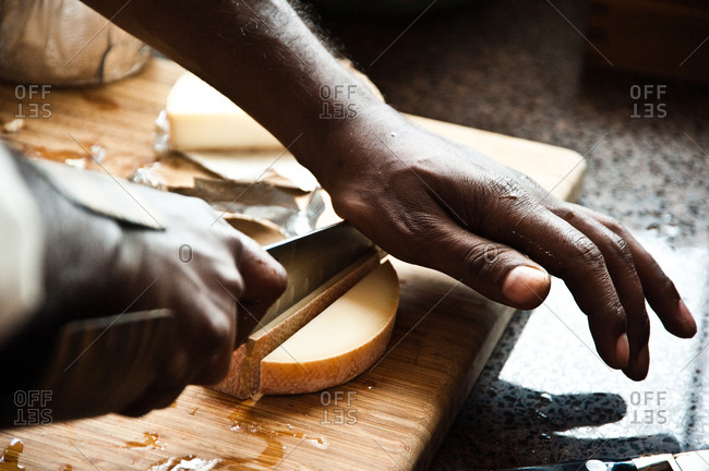 Chef slicing cheese on wooden cutting board