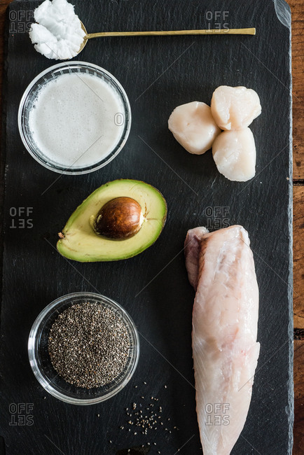 Overhead view of monkfish, sea scallops, chia seeds and avocado on slate