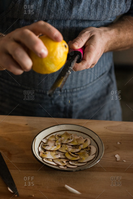 Chef grating lemon rind over bowl of sliced mushrooms