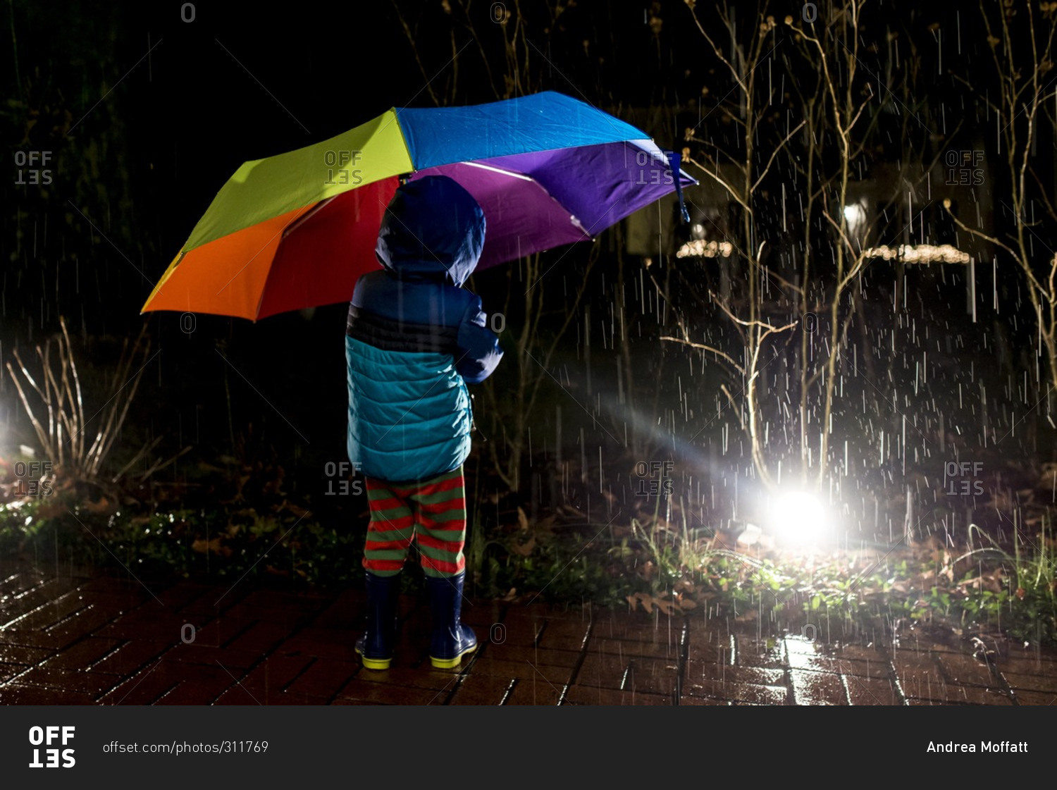 Boy with rainbow umbrella at night in rain