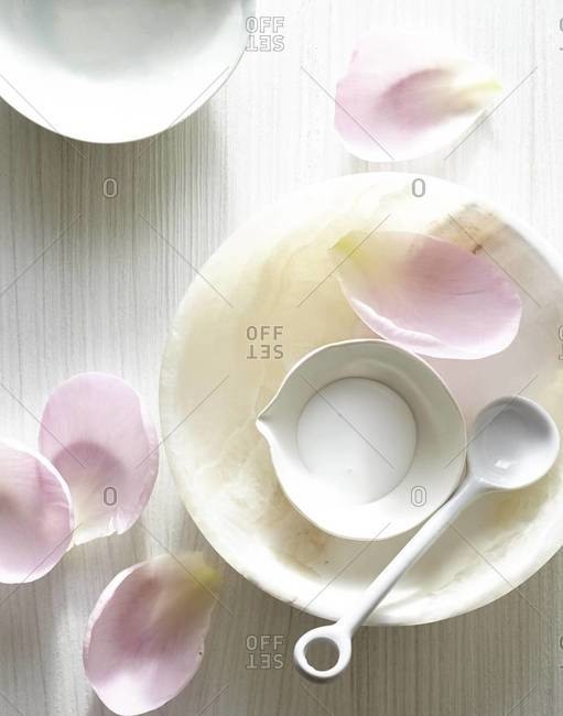 Flower petals scattered around dish containing spa facial cream