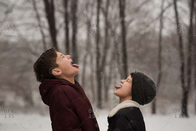 Brothers facing each other and catching snowflakes in their mouths
