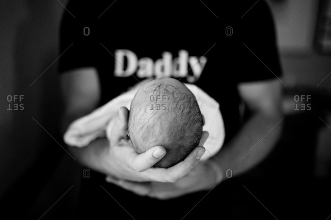 Newborn baby in hands of father in "Daddy" shirt