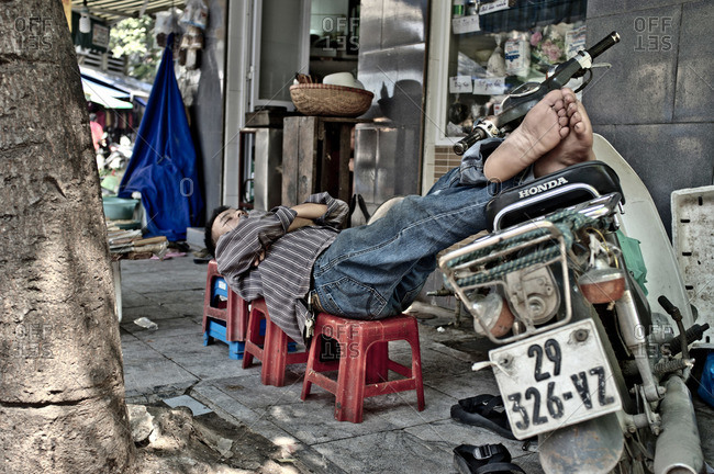 Hanoi, Vietnam - September 25, 2011: Man lying across stools in Vietnam