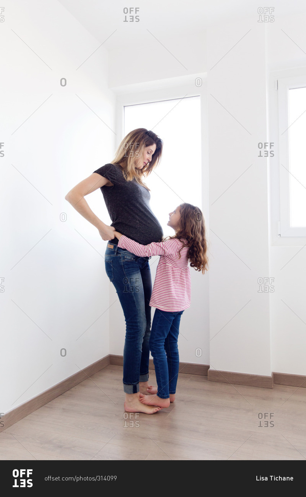 Daughter hugging her pregnant mother in corner of white room