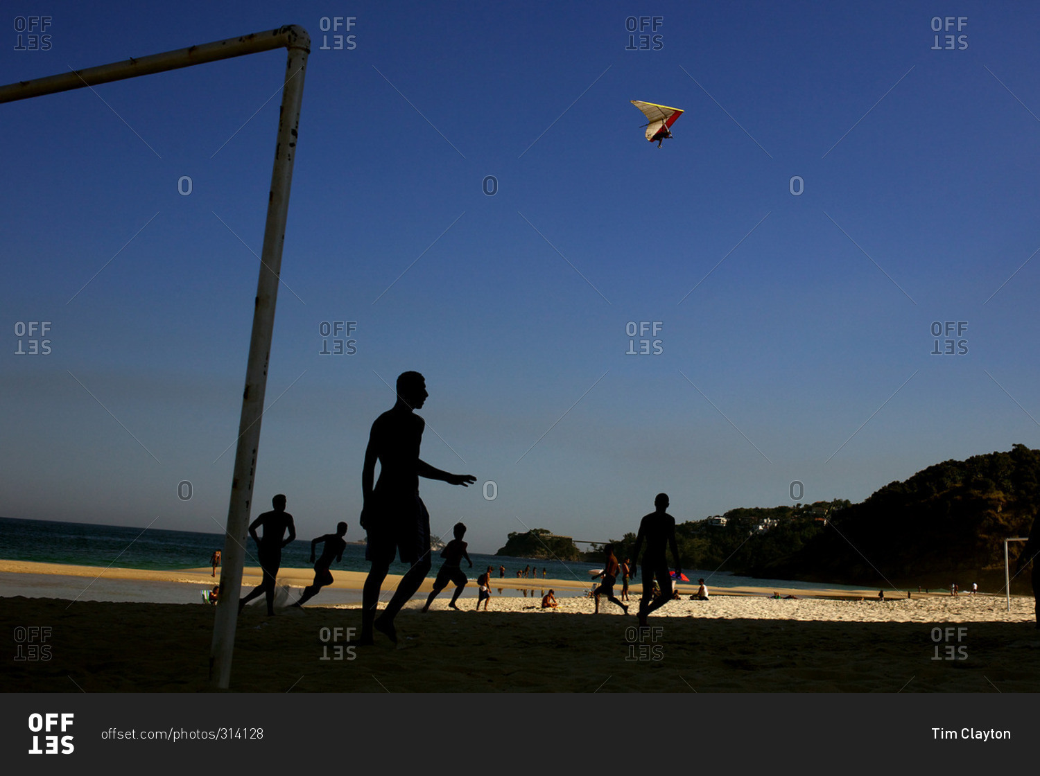 A hang glider in the late afternoon light above football players at Sao Conrado beach