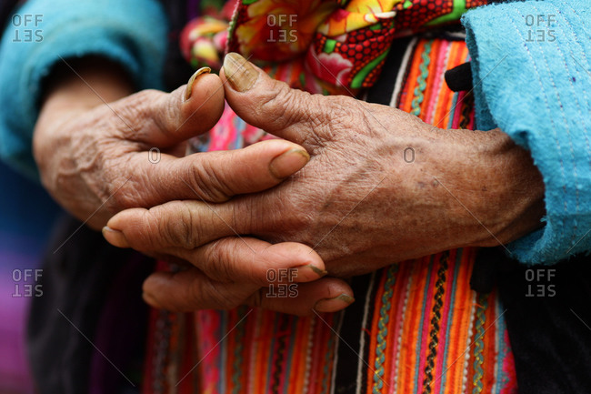 The hands of an elderly woman against her colorful skirt at the Lung Khau Nhin Market, Vietnam