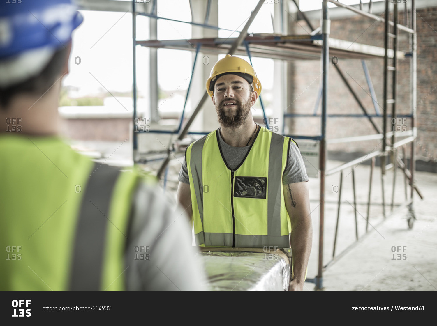 Closeup of two construction workers carrying item in construction site