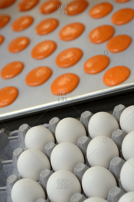 A dozen eggs next to a baking sheet covered with orange treats