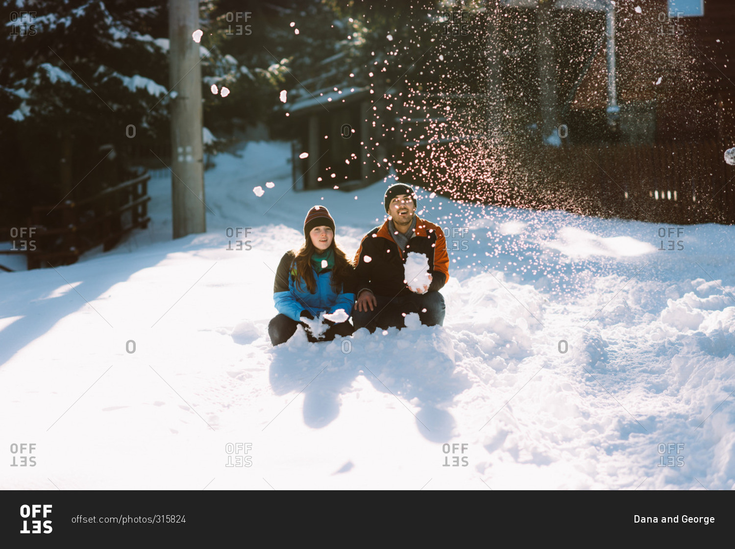 Young couple sit together watching the snow he has thrown into the air