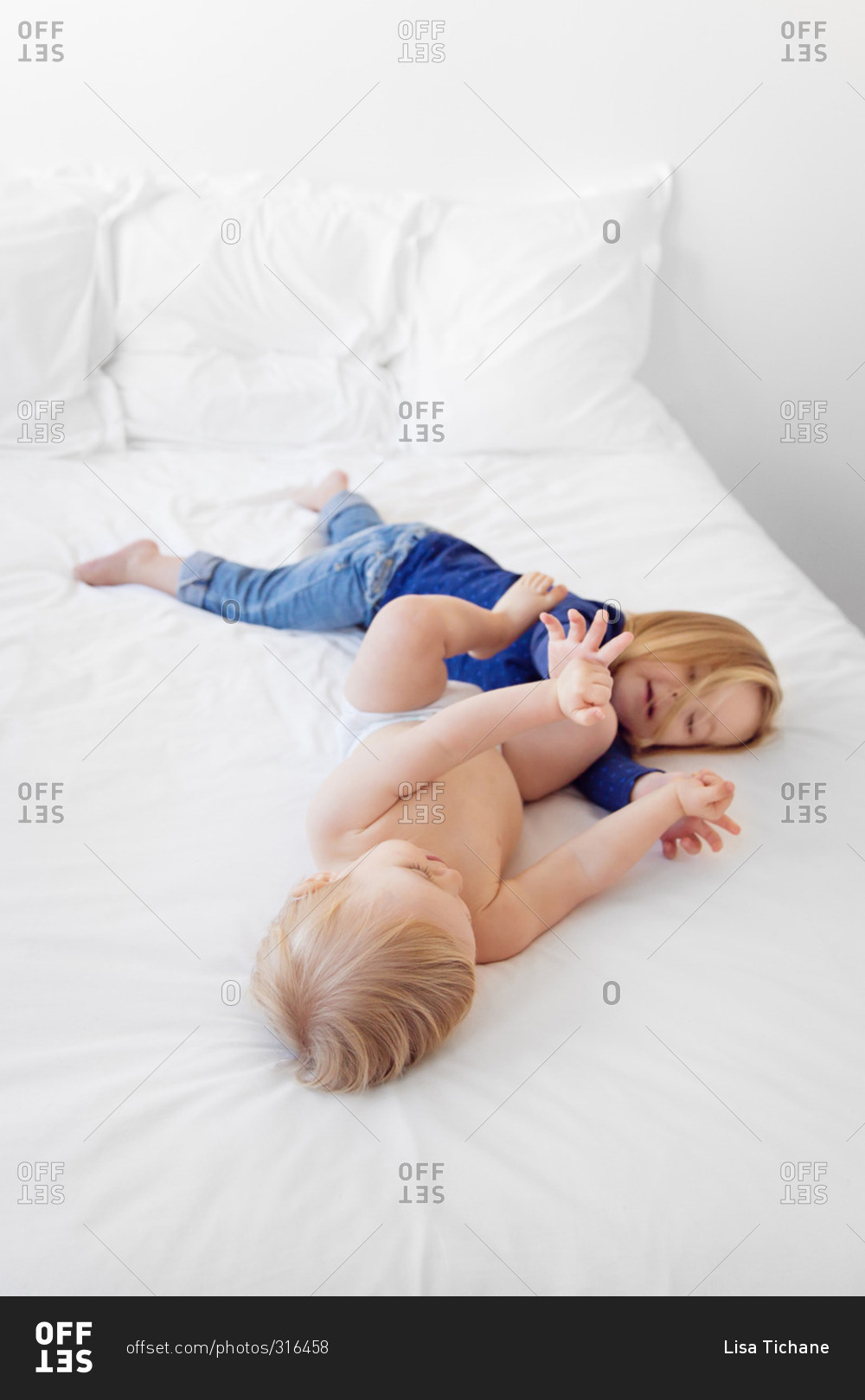 Brother and sister wrestling on a white bed