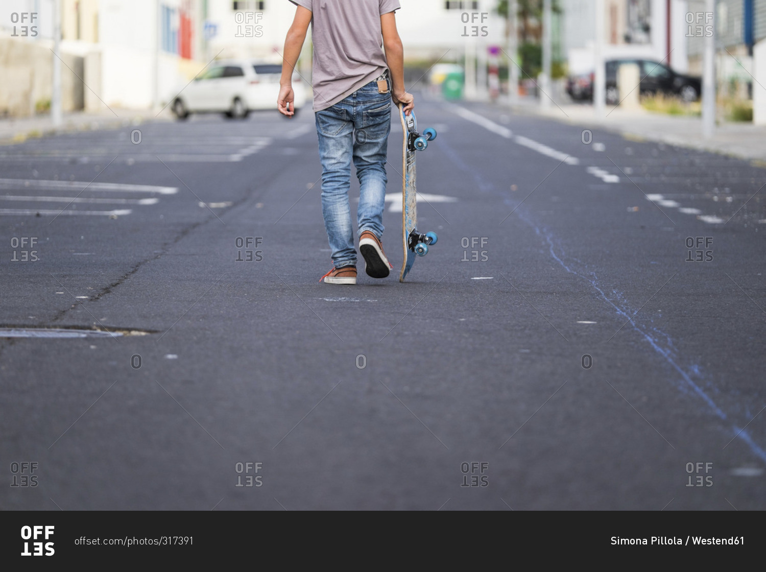 Back view of boy carrying his skateboard on a street stock photo OFFSET