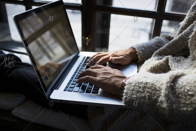 Close up of man in wooly sweater using laptop in window seat