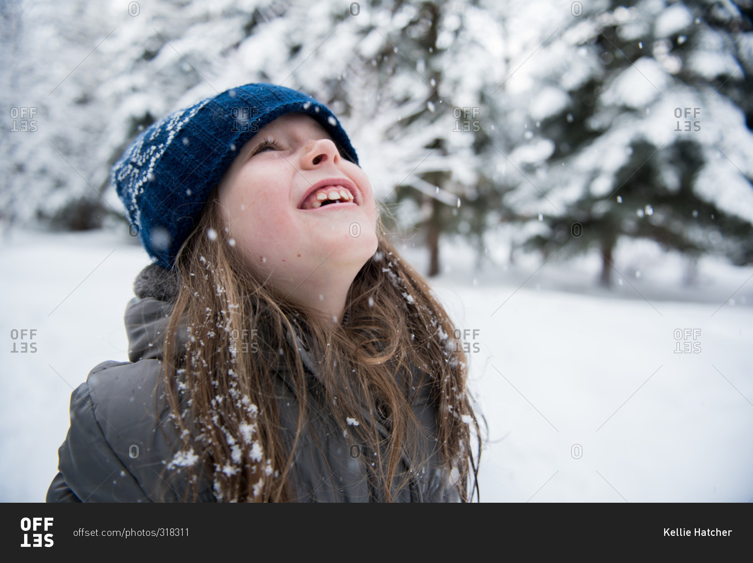 Happy young girl looking up at the snow falling stock photo - OFFSET