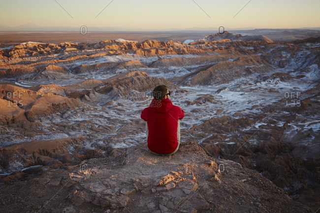 Man sitting at the edge of a cliff overlooking the sunset in a desert ...