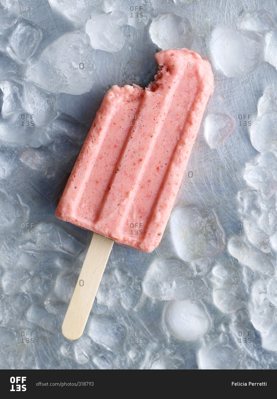 A strawberry popsicle with a bite missing