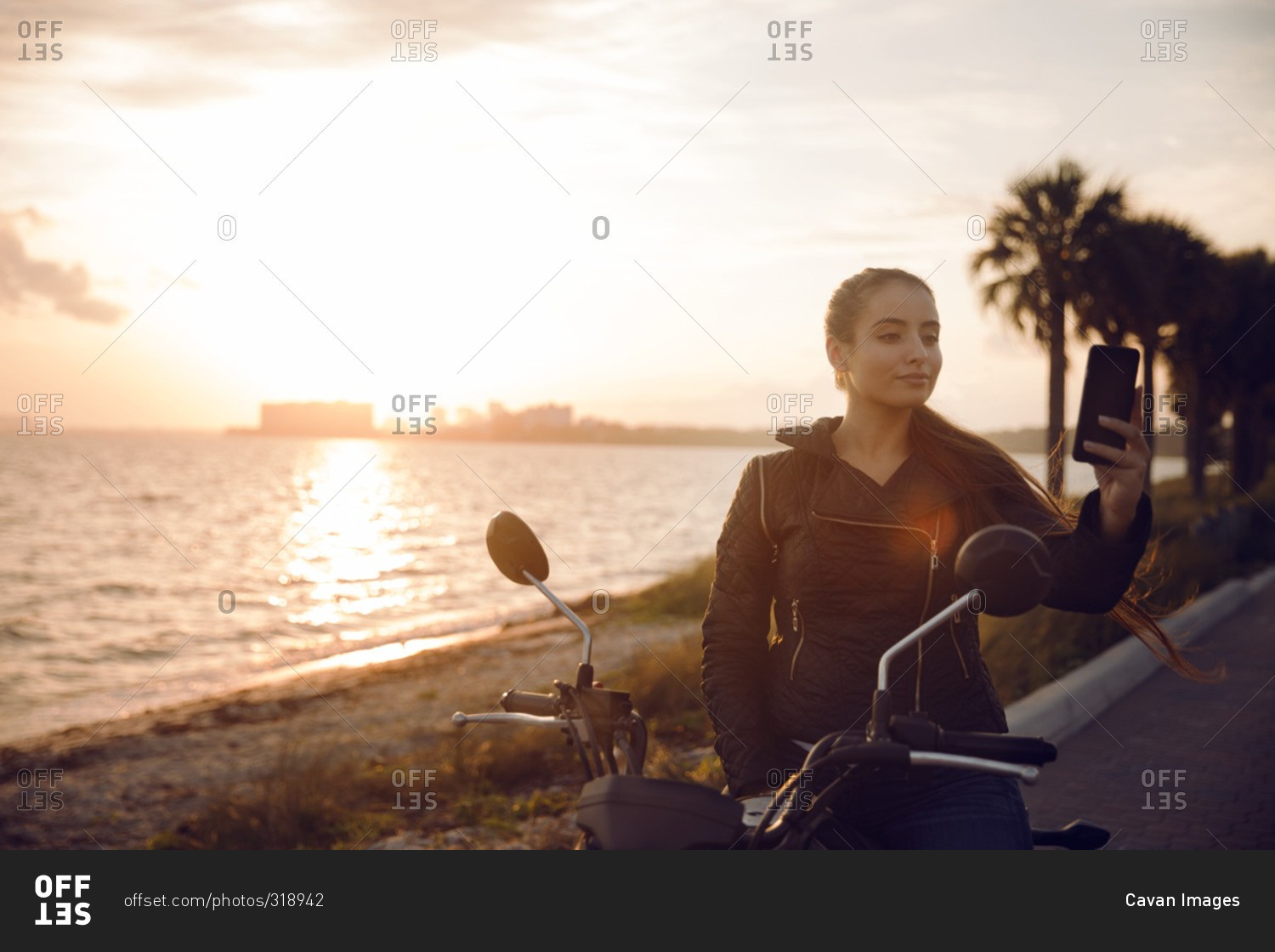 Woman by motorcycle holding smartphone