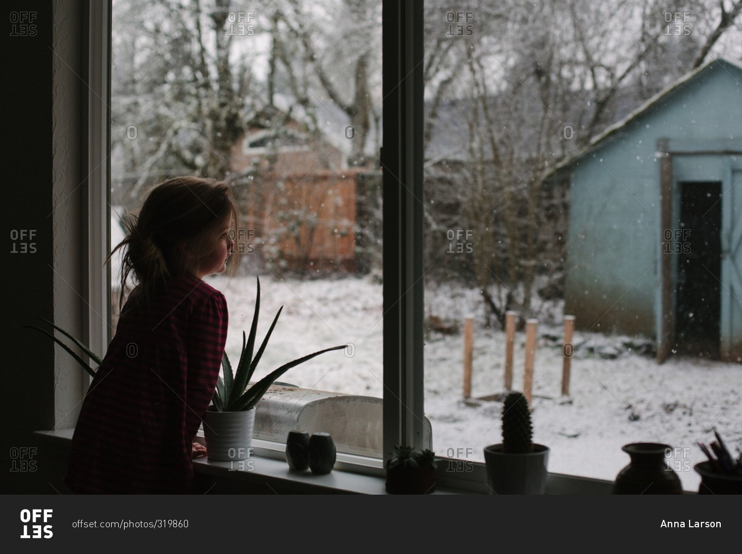 Girl leans on windowsill to watch snow falling in her backyard
