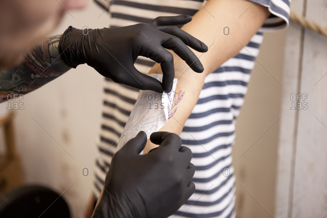 Hands of tattooist removing stencil from forearm of a client