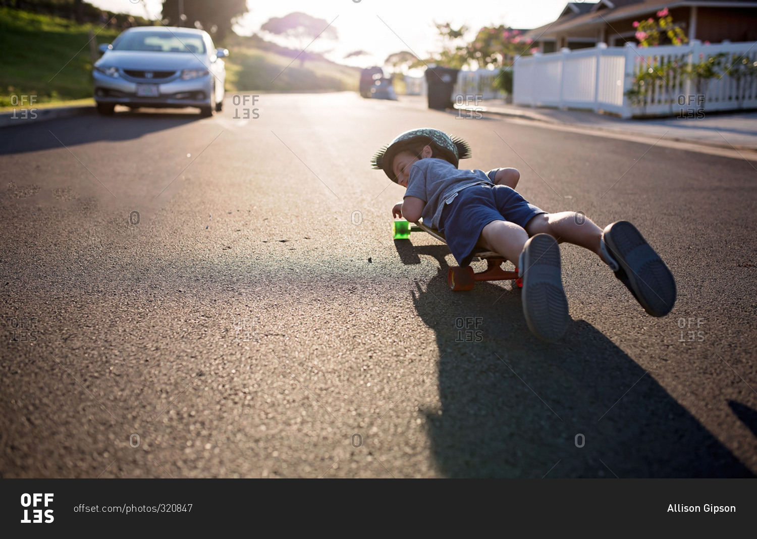 Boy lying flat on a skateboard rolling down a street
