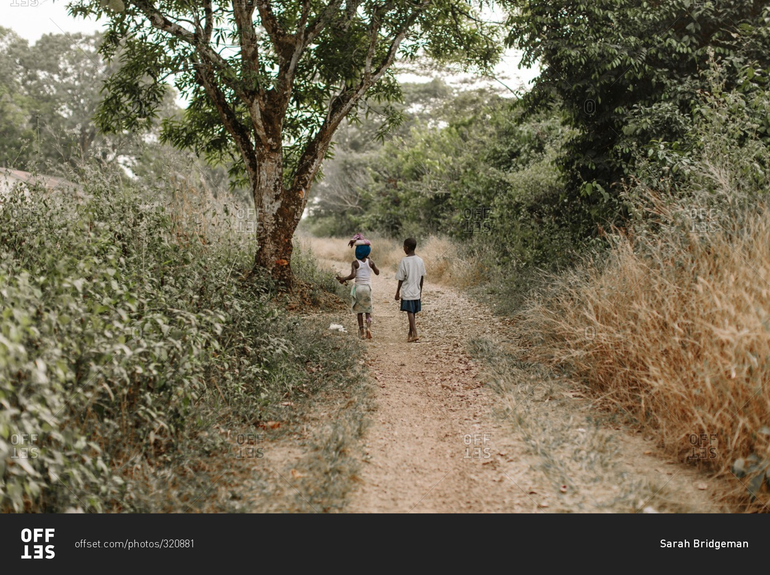 Two children walking down a dirt pathway in the rural countryside of Sierra Leone