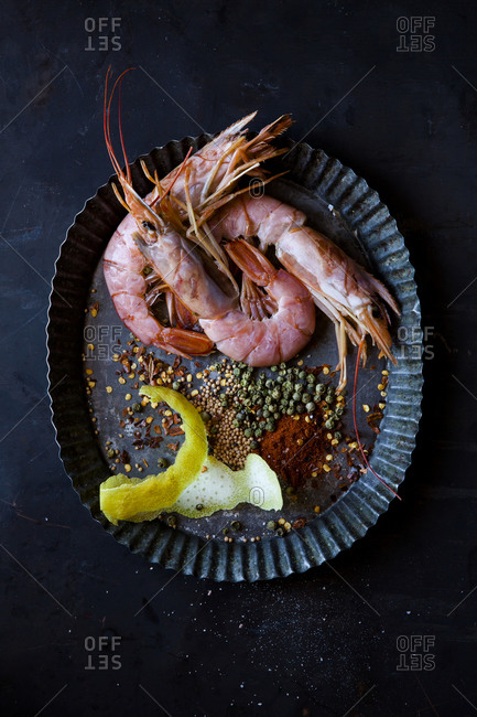 Overhead view of whole fresh prawns on plate with spices and lemon rind