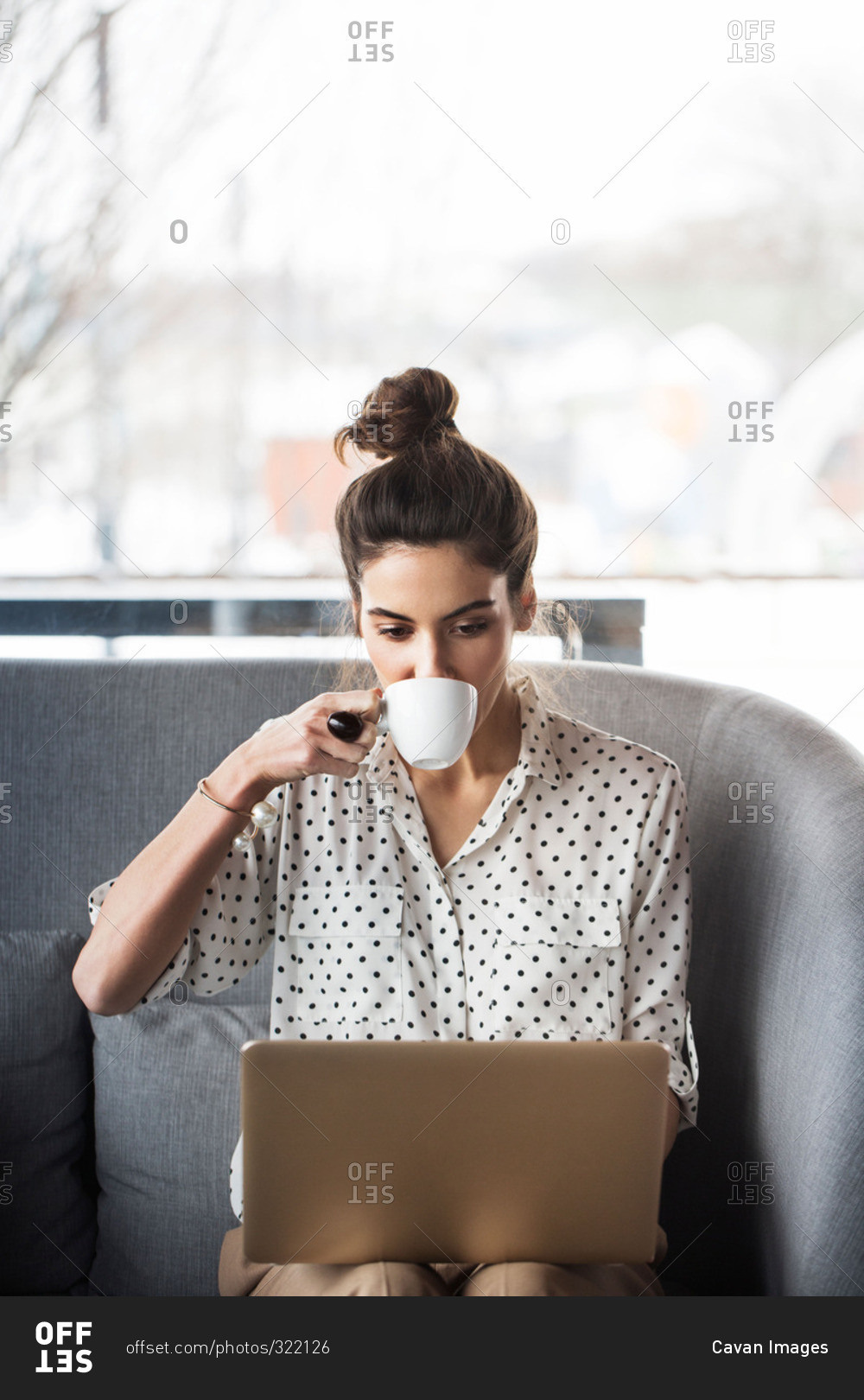 Woman sipping coffee with laptop stock photo - OFFSET